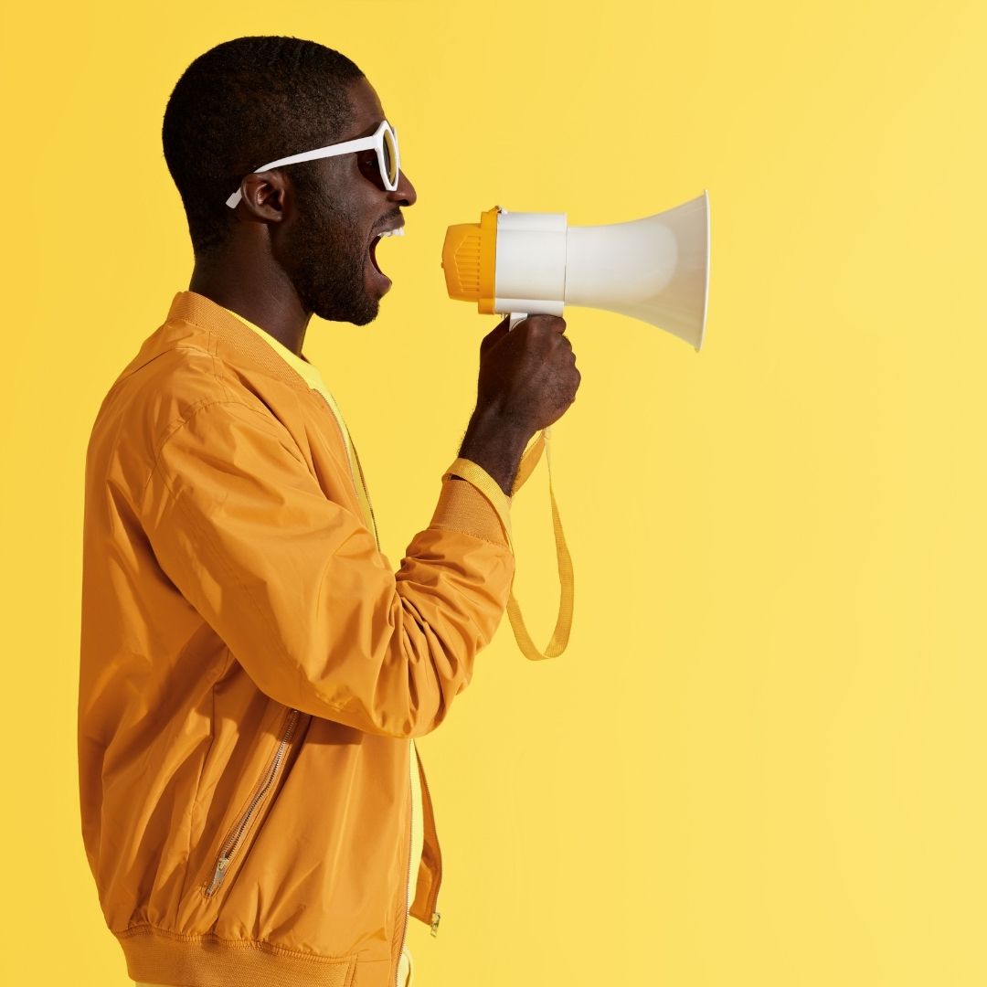 Man in yellow jacket shouting into a megaphone against a yellow background for advertising purposes.